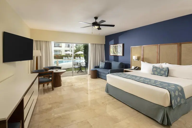 Une chambre lumineuse avec un grand lit et un coin salon donnant sur une piscine.