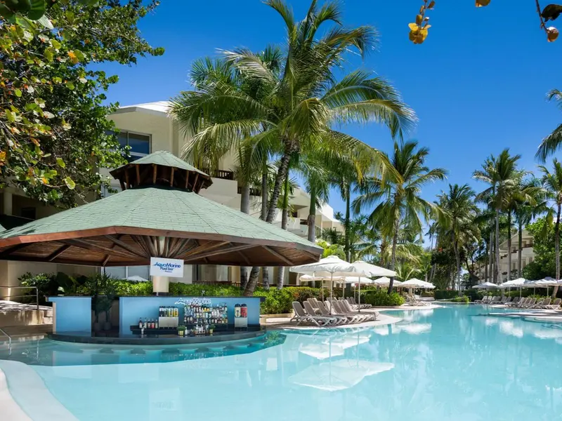 Un bar au bord d'une piscine turquoise, entouré de végétation tropicale et de transats.