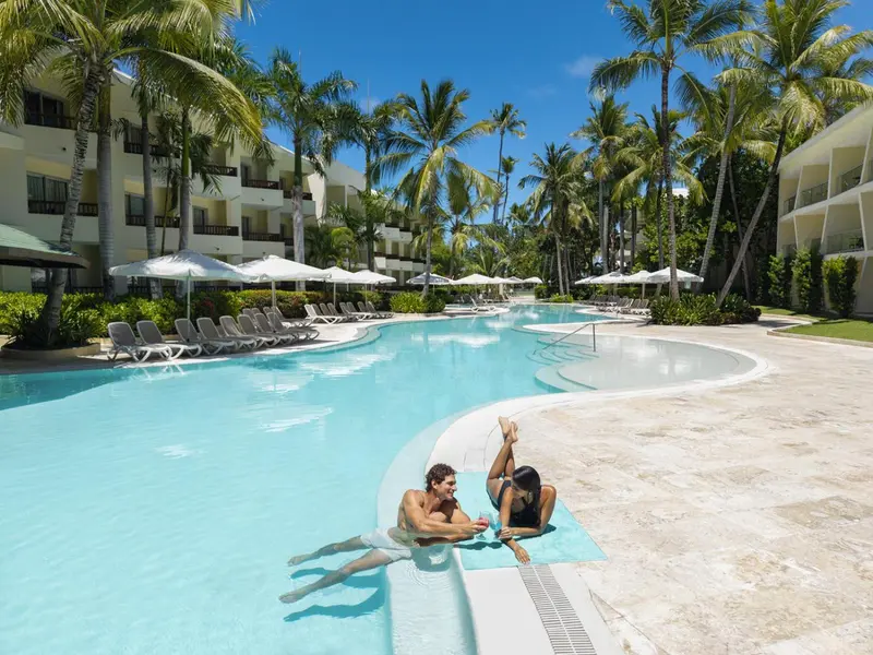 Deux personnes se détendent au bord d'une piscine sinueuse dans un complexe hôtelier tropical.