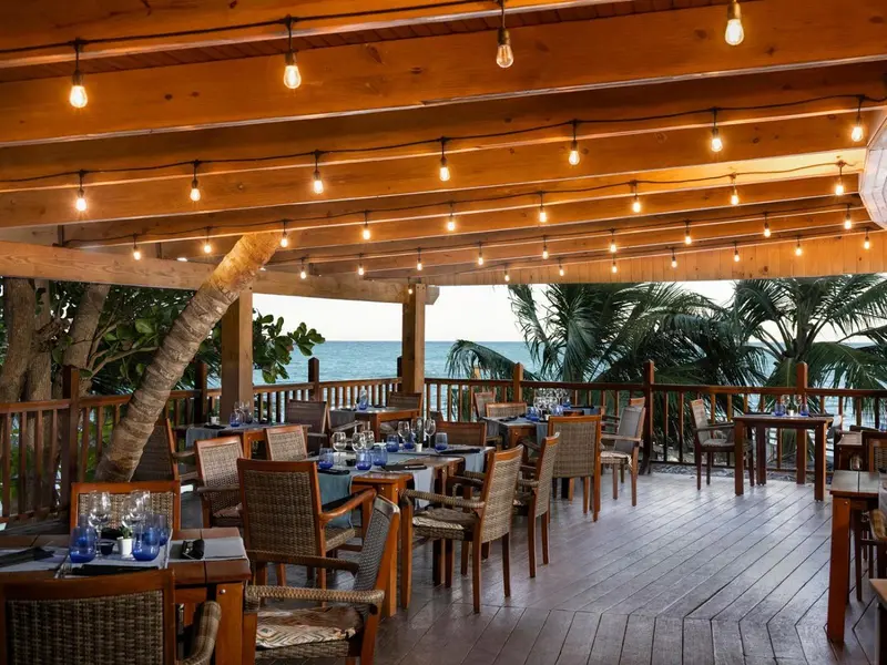 Terrasse de restaurant en bois avec tables dressées face à la mer.