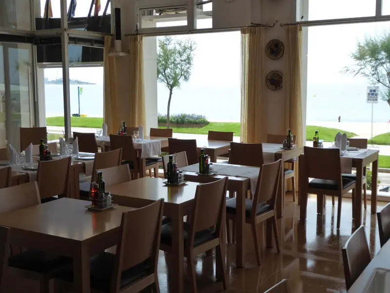 Une salle de restaurant lumineuse avec des tables dressées face à la mer.