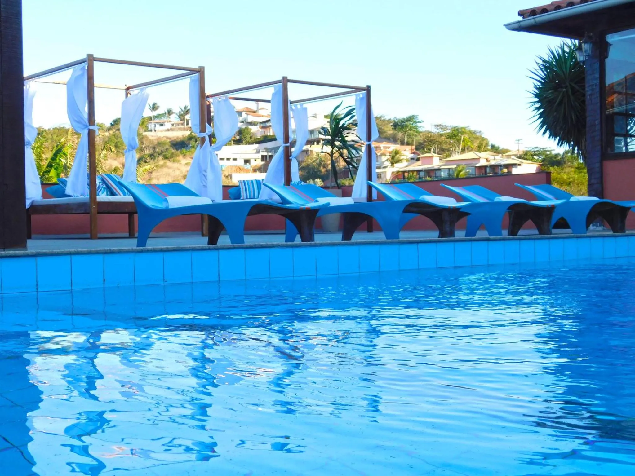 Transats bleus alignés au bord d'une piscine turquoise sous un ciel bleu.
