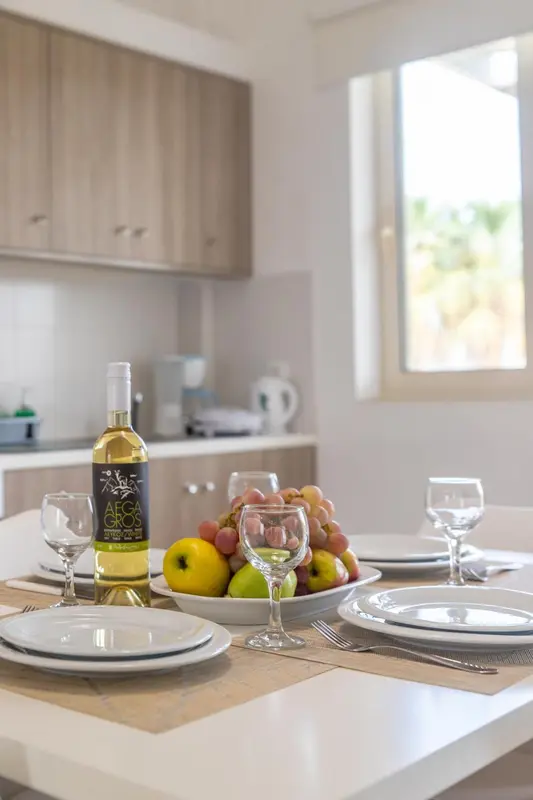 Une table est dressée avec des fruits, des verres et des assiettes dans une cuisine lumineuse.