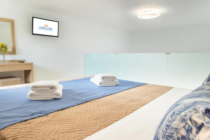 Une chambre lumineuse avec un lit soigneusement fait et une télévision murale.