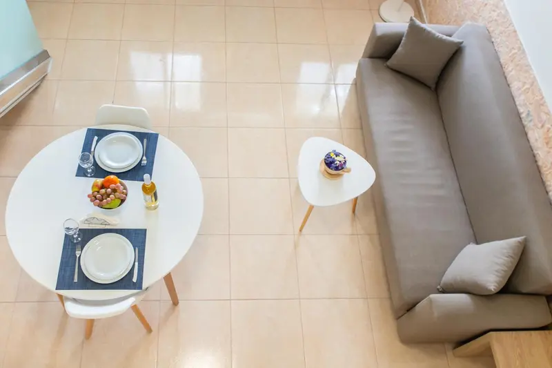 Une table ronde est mise avec de la vaisselle et des fruits frais, à côté d'un canapé gris et de coussins.