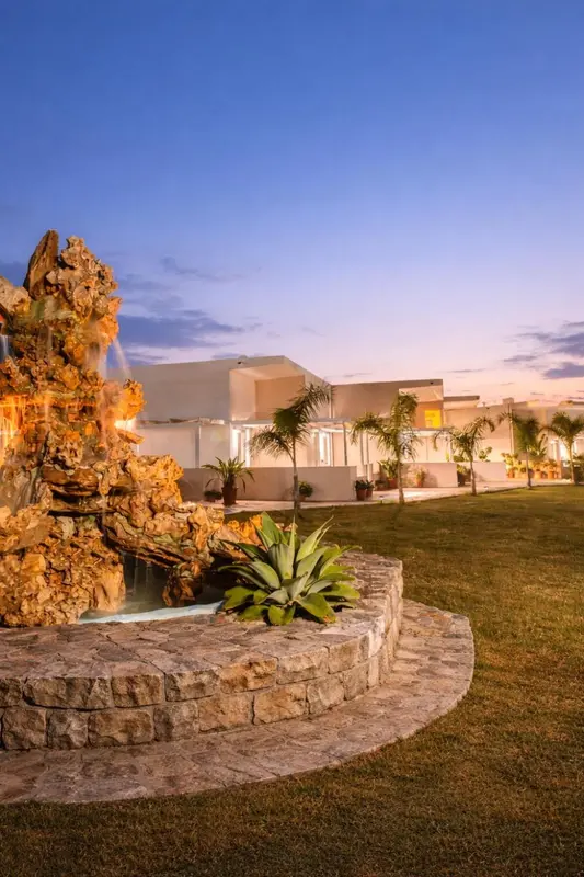 Bâtiment éclairé avec une cascade rocheuse au premier plan et une pelouse verdoyante.