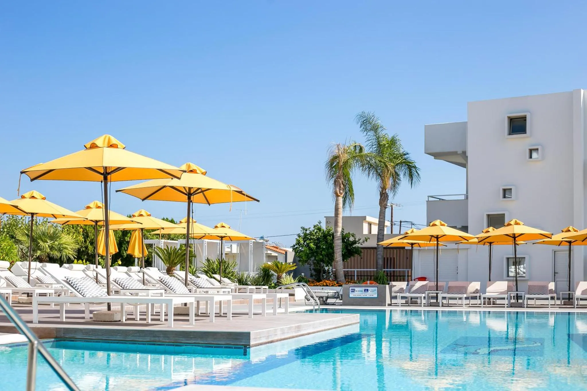 Transats et parasols jaunes bordent une piscine turquoise dans un complexe hôtelier.