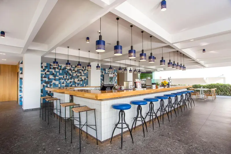 Un long comptoir de bar en bois et carrelage blanc est aligné de tabourets hauts.