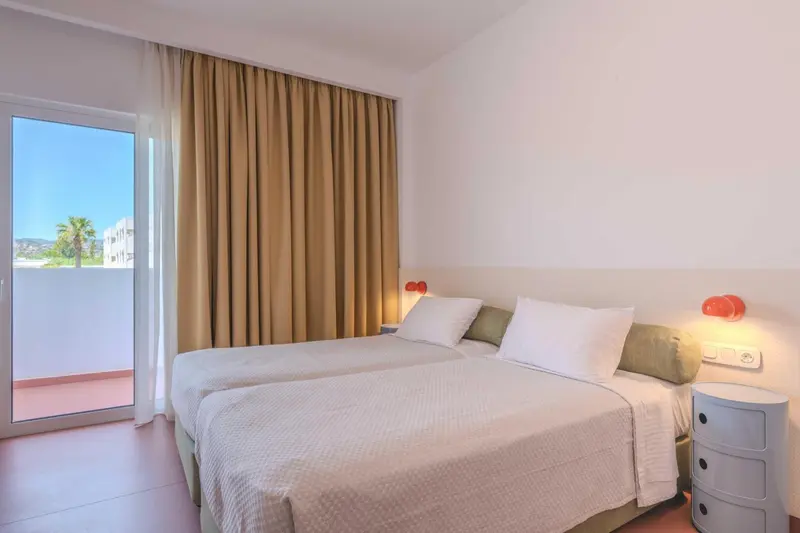 Chambre lumineuse avec deux lits simples et vue sur l'extérieur.