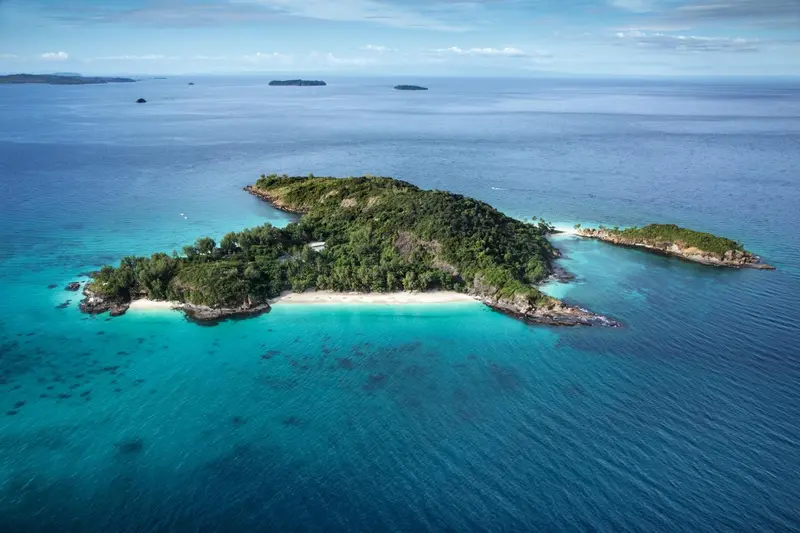 Vue aérienne d'une île tropicale bordée de plages de sable blanc et entourée d'eaux turquoise.