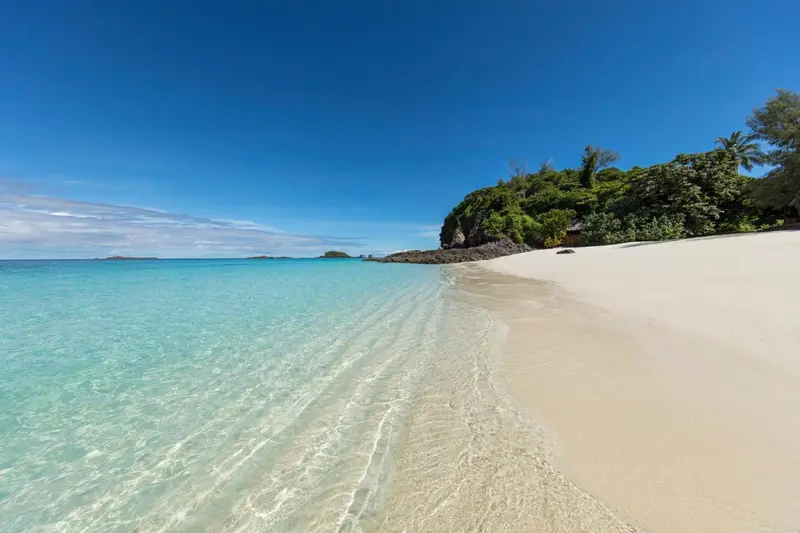 Plage de sable blanc bordée d'une eau turquoise et d'une végétation luxuriante.
