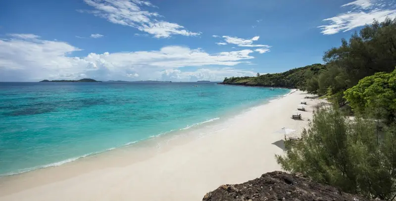 Une plage de sable blanc bordée d'une eau turquoise et de végétation luxuriante.