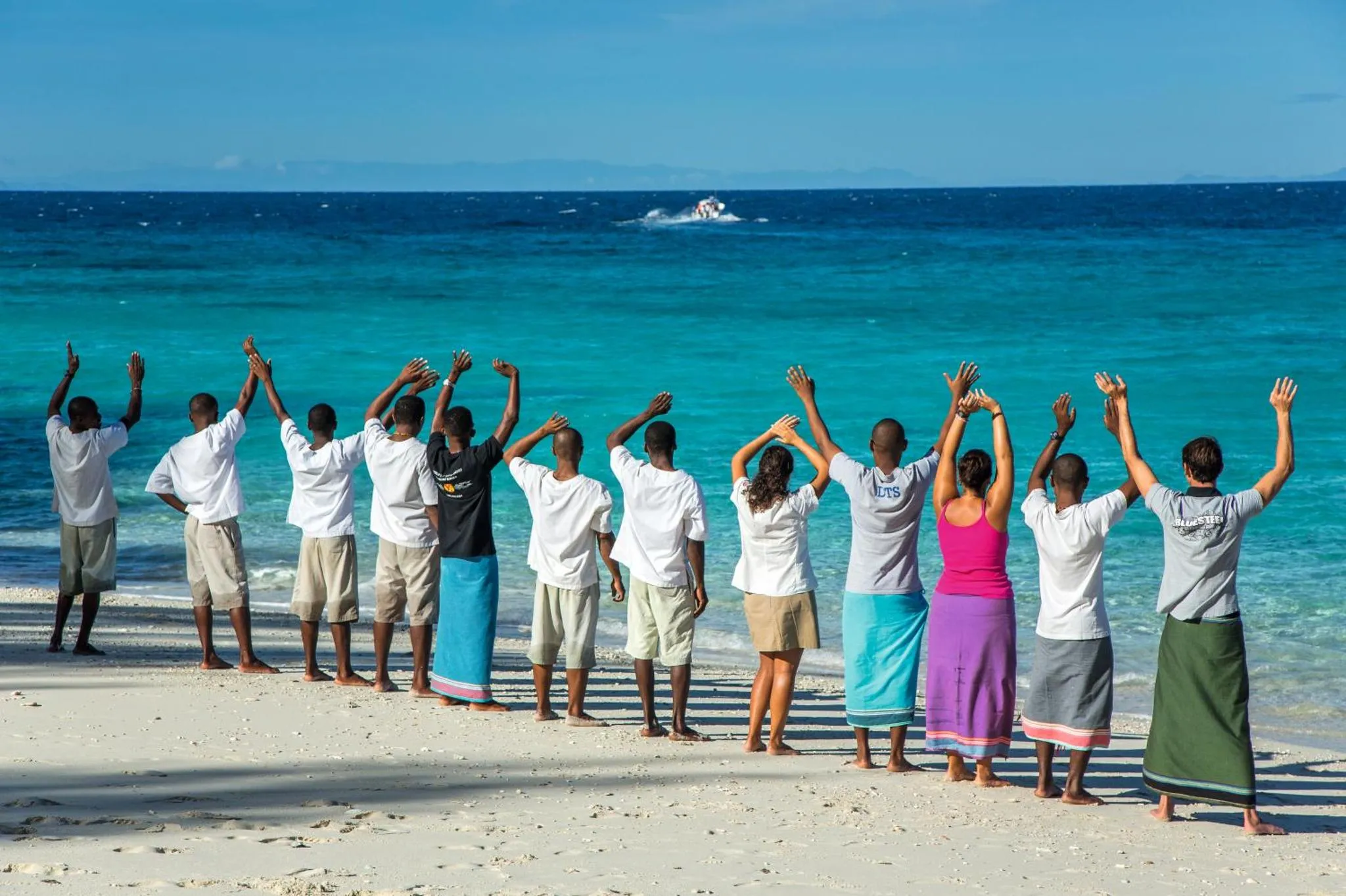 Groupe de personnes se tenant par la main sur une plage de sable blanc face à la mer turquoise.