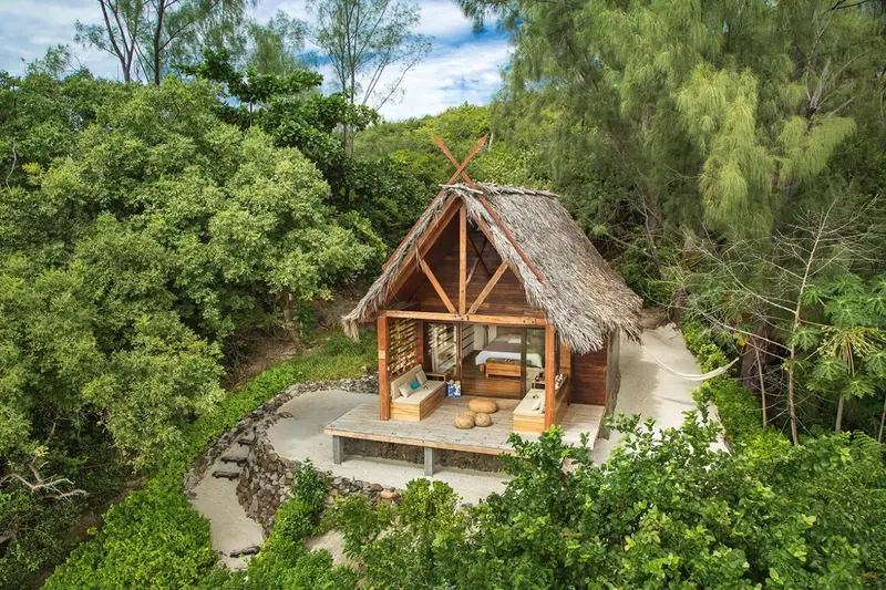 Cabane en bois sur pilotis avec terrasse et mobilier de jardin.