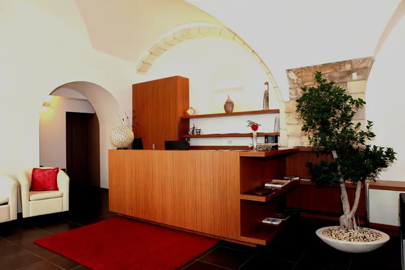 Un comptoir d'accueil en bois se trouve dans un hall d'entrée décoré d'arches et de plantes.