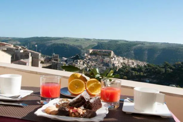 Une table avec des pâtisseries, des fruits et des boissons offre une vue sur un paysage urbain et montagneux.