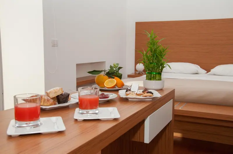 Une table basse en bois présente un petit déjeuner avec des jus d'orange, des viennoiseries et des fruits frais dans une chambre.