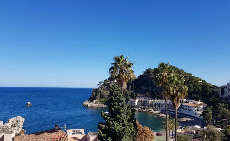 Vue d'une crique bordée de végétation et de bâtiments blancs.