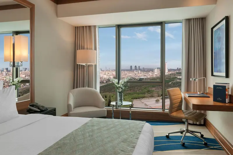 Une chambre lumineuse avec un lit et un espace bureau donnant sur une vue urbaine.