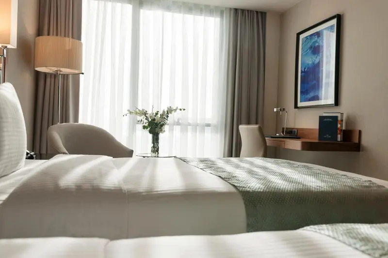 Une chambre lumineuse avec un lit fait et un coin lecture près de la fenêtre.