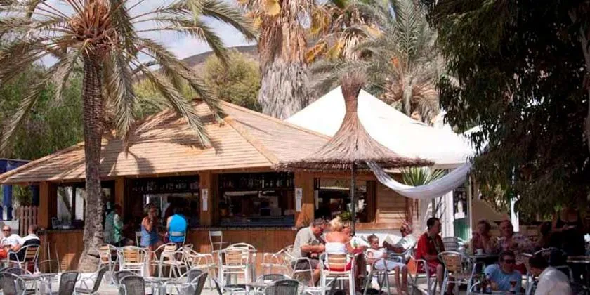 Un bar de plage ombragé accueille des clients sur des tables et des tabourets.