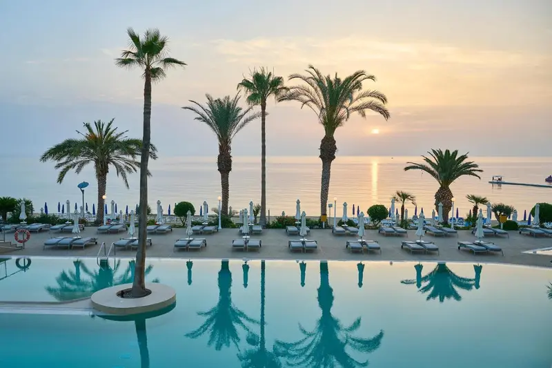 Plages de sable fin et palmiers au bord d'une piscine turquoise au coucher du soleil.