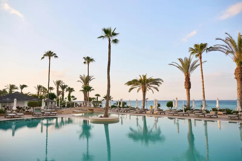 Une piscine turquoise reflète les palmiers et le ciel bleu.