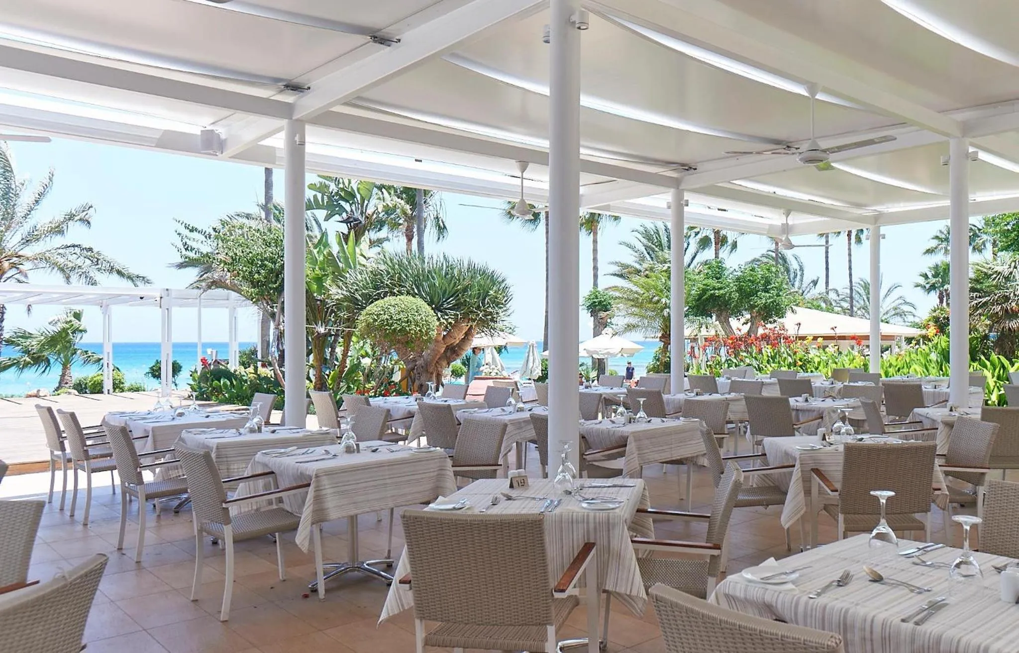 Une terrasse ombragée avec des tables dressées face à la mer.