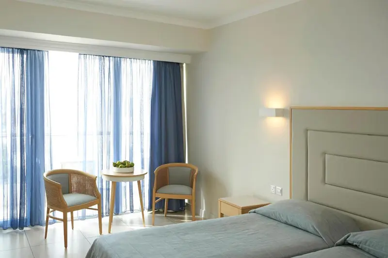 Une chambre lumineuse avec un lit et deux fauteuils près d'une fenêtre.