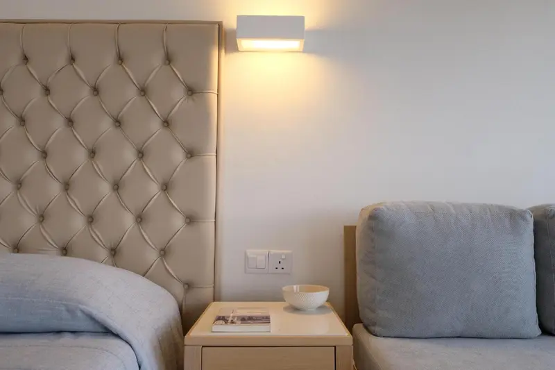 Une tête de lit capitonnée beige domine une chambre lumineuse.