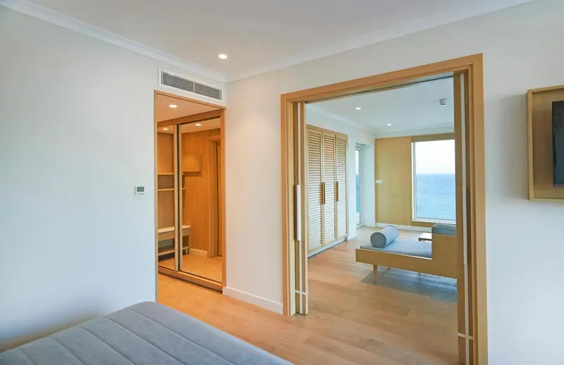 Une chambre d'hôtel lumineuse s'ouvre sur un espace de détente avec vue sur la mer.