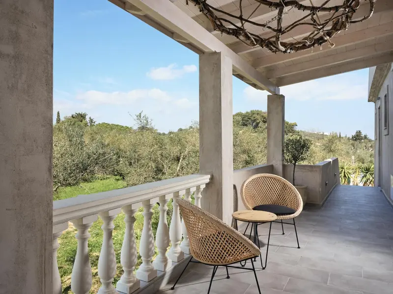 Terrasse ombragée avec mobilier en rotin donnant sur un paysage verdoyant.