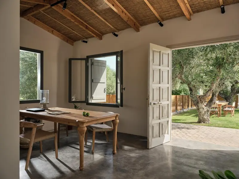 Une table en bois est placée devant une fenêtre ouverte sur un jardin verdoyant.