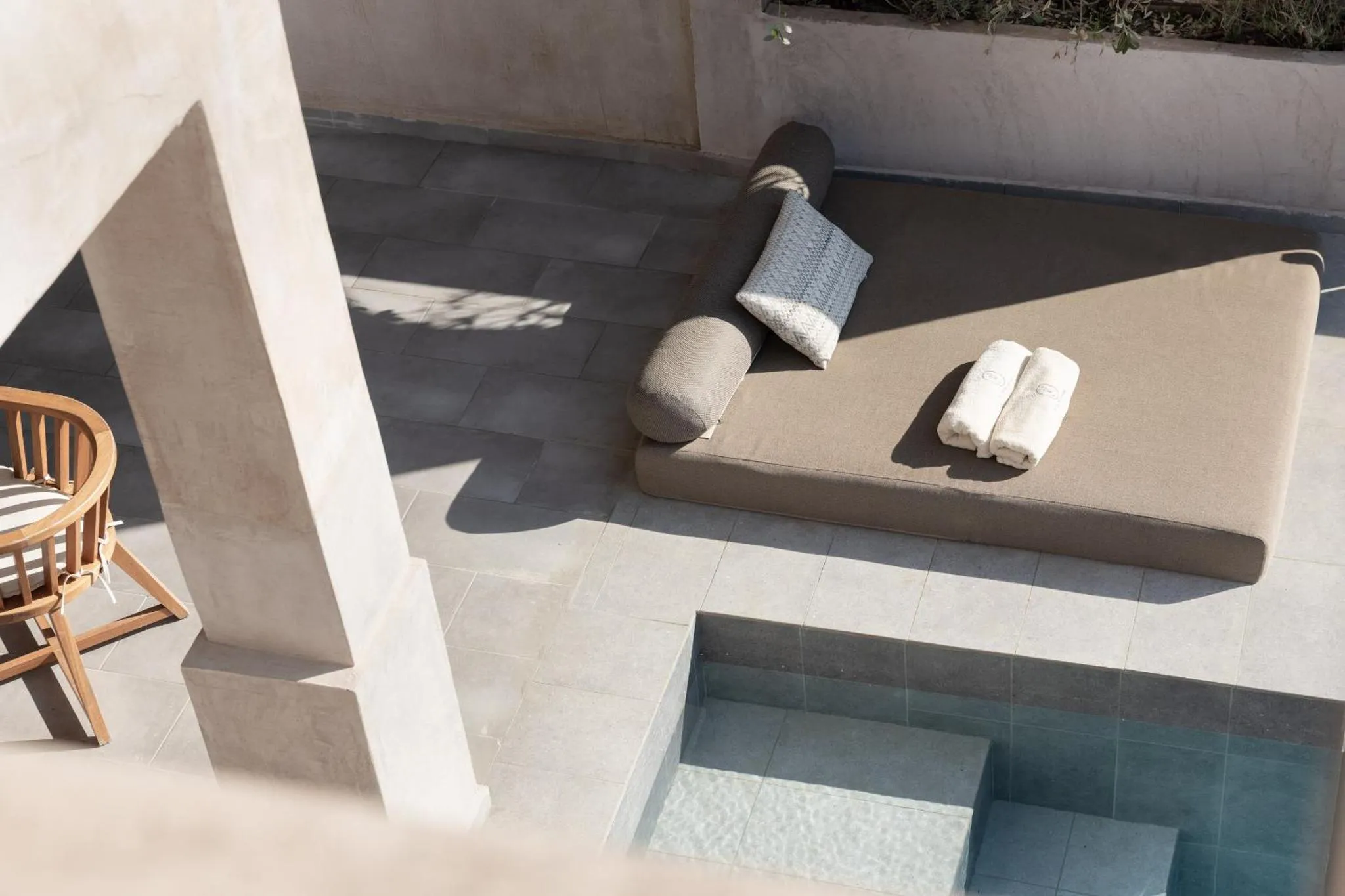 Transats et coussins sur une terrasse carree avec une piscine turquoise.