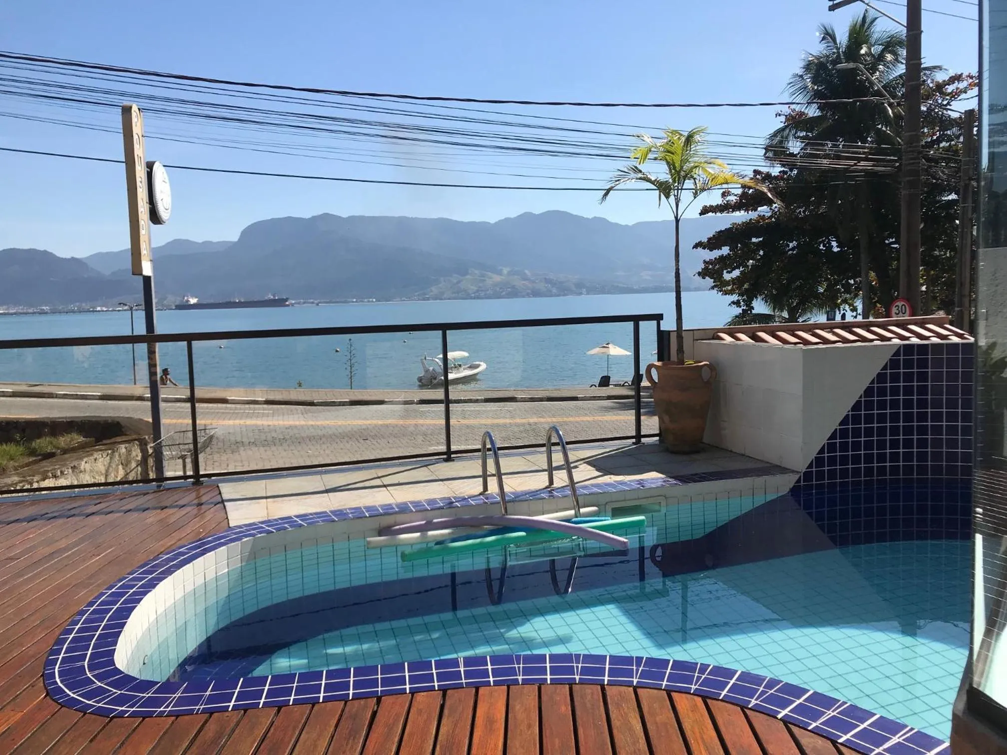 Petite piscine avec terrasse en bois et vue sur la mer.