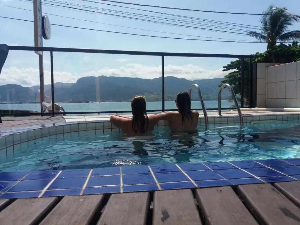 Deux personnes se tiennent au bord d'une piscine avec vue sur la mer et les montagnes.