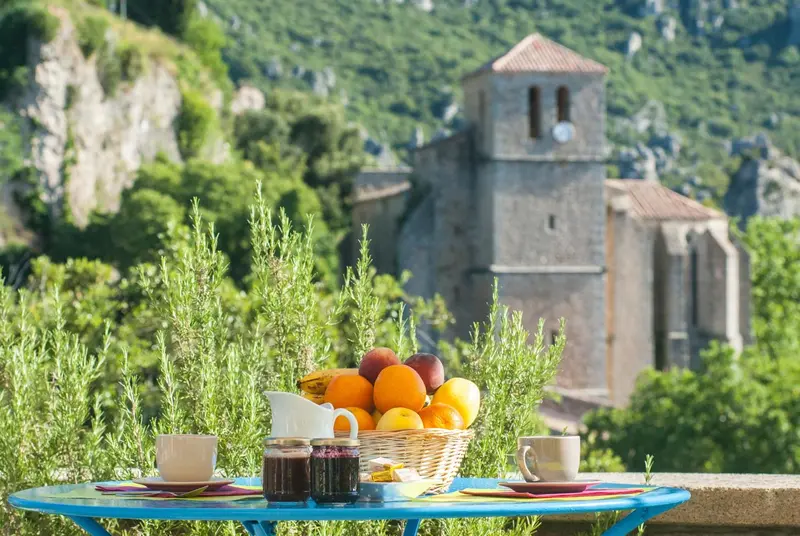 Nature morte de fruits frais et de confiture sur une table bleue avec une vue sur un village en arrière-plan.