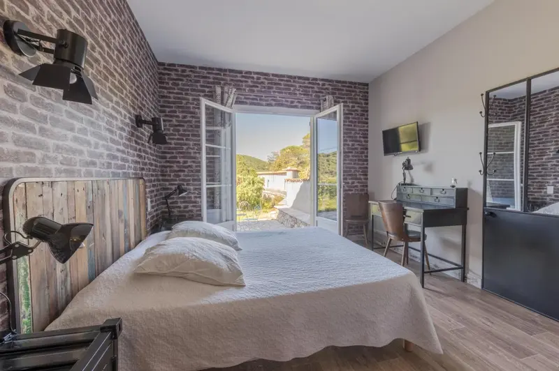 Une chambre lumineuse avec un lit double et un bureau donnant sur un paysage verdoyant.