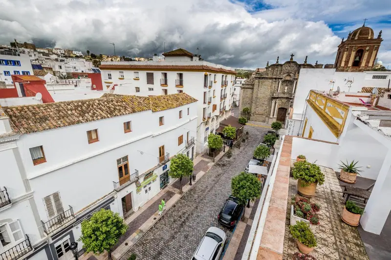 Vue aérienne d'une ruelle pavée bordée de bâtiments blancs et de quelques arbres.