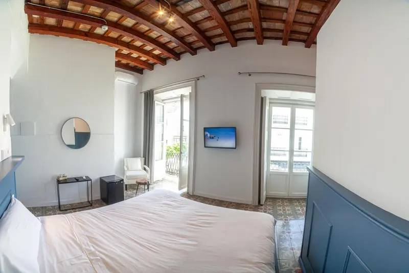 Une chambre lumineuse avec un lit blanc et un accès à un balcon.