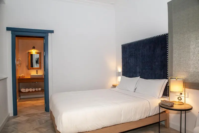 Une chambre lumineuse avec un grand lit et un espace lavabo ouvert.