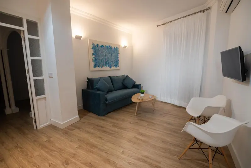 Un salon clair avec un canapé bleu et deux fauteuils blancs.