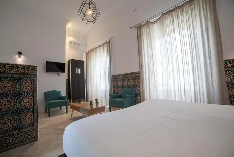 Une chambre lumineuse avec un lit blanc et deux fauteuils verts.