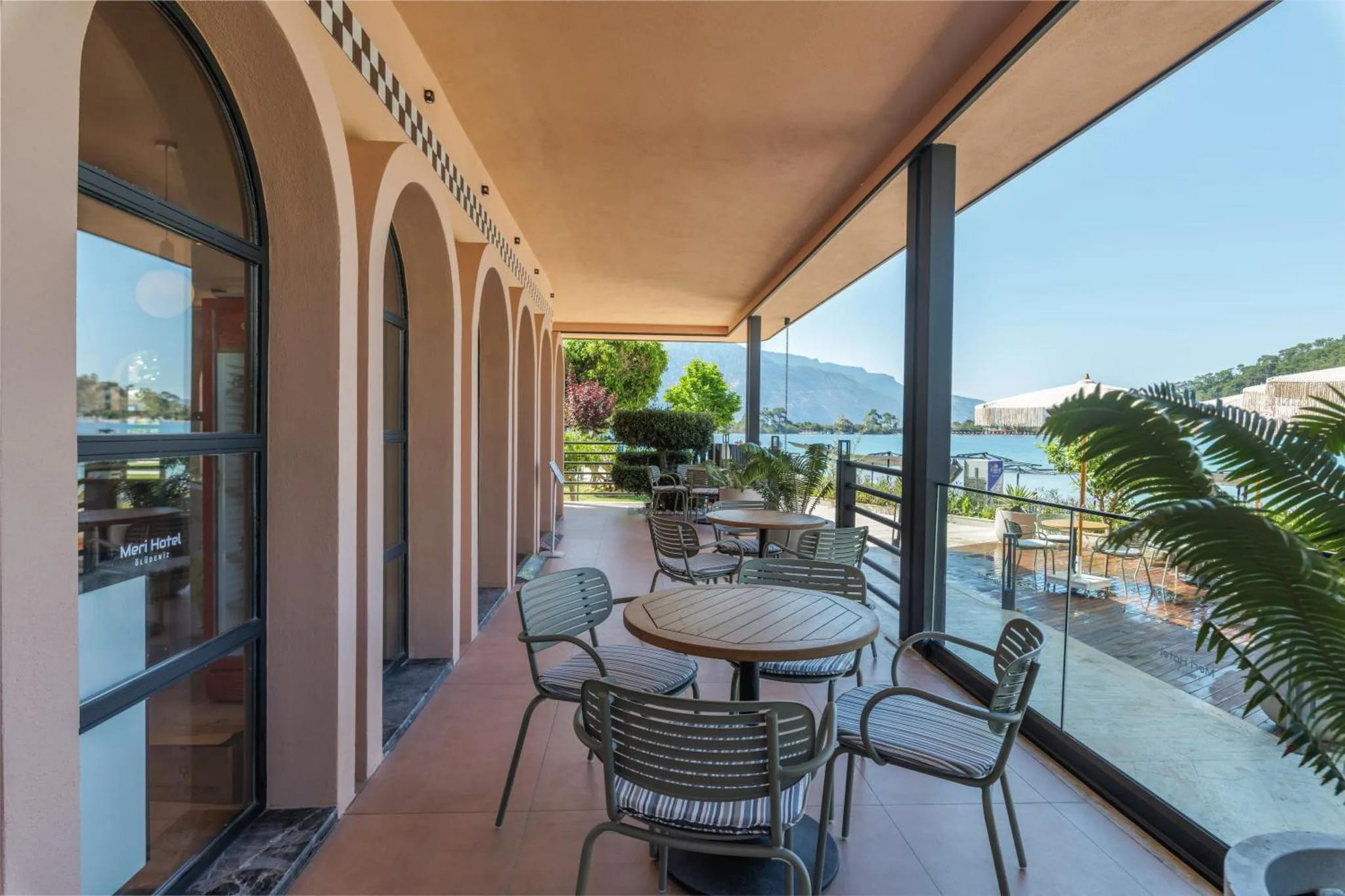 Terrasse ombragée avec tables et chaises donnant sur la mer.