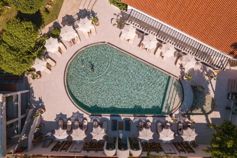 Vue aérienne d'une piscine de forme organique entourée de transats blancs sous des parasols.