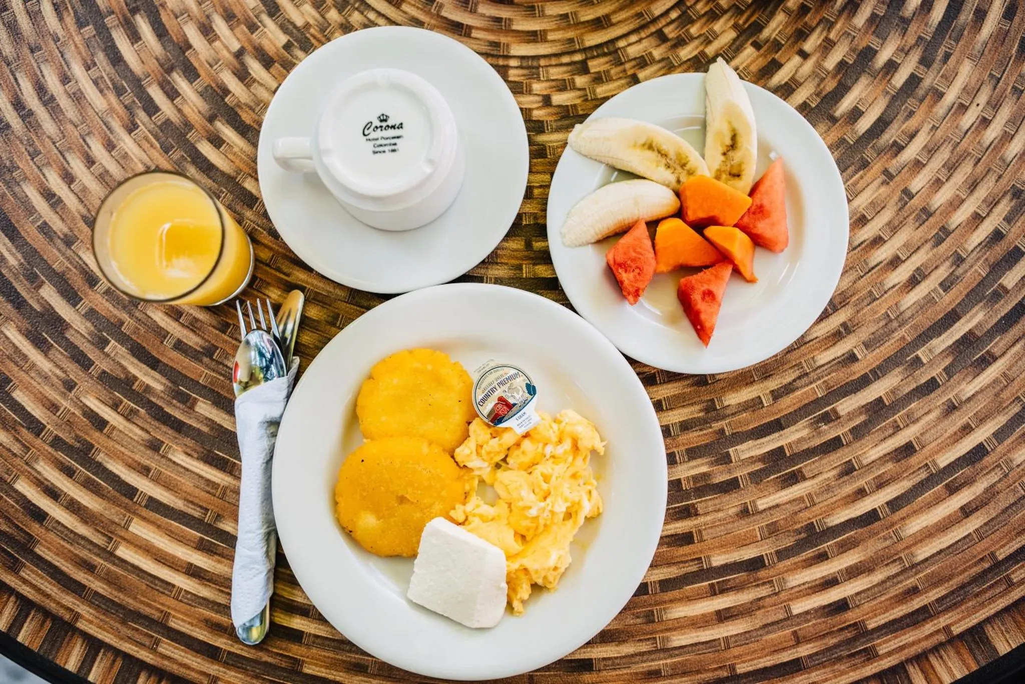 Une table ronde en bois présente un petit-déjeuner avec des fruits frais et des œufs brouillés.