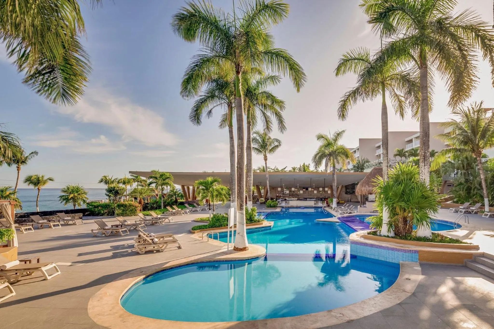 Piscine d'hôtel avec transats et végétation tropicale en bord de mer.