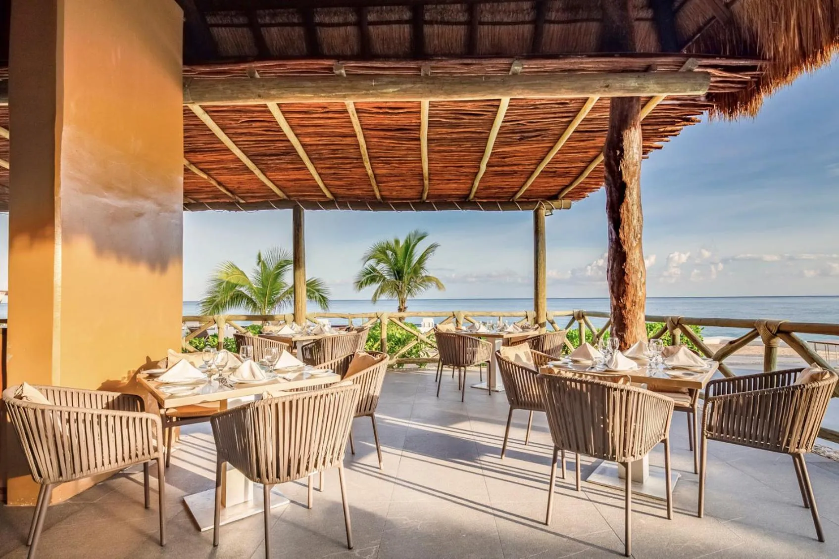 Terrasse ombragée avec tables dressées face à la mer.