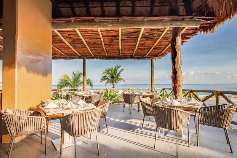 Terrasse ombragée avec tables dressées face à la mer.