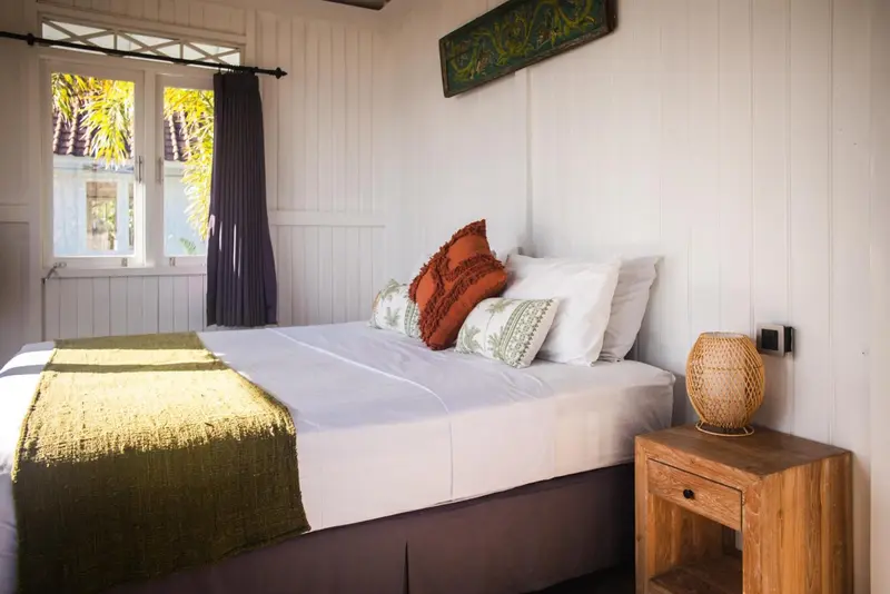 Une chambre lumineuse avec un lit recouvert d'une couverture verte et de coussins décoratifs.